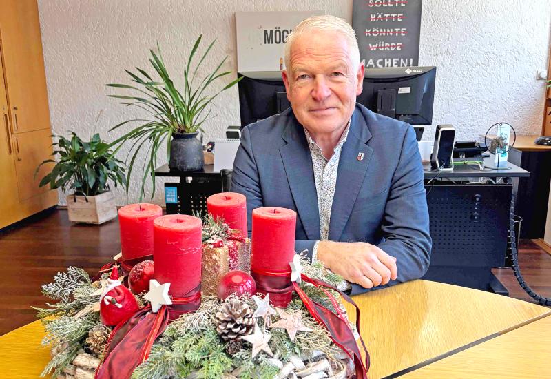 Bürgermeister Christoph Dellmans sitzt hinter einem Adventskranz mit roten Kerzen an einem Tisch in seinem Büro